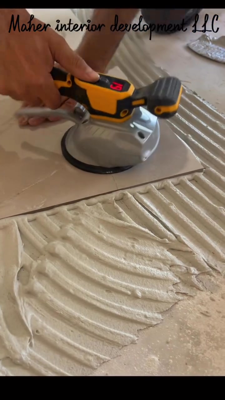 Large-format tile being set into notched thinset with a vibrating leveling tool